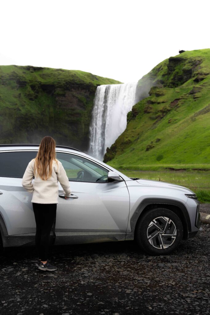 A woman entering her rental vehicle in front of the world famous skogafoss